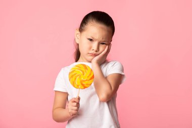 Sevimli Asyalı kız lolipop tutuyor ve yanağına dokunuyor.