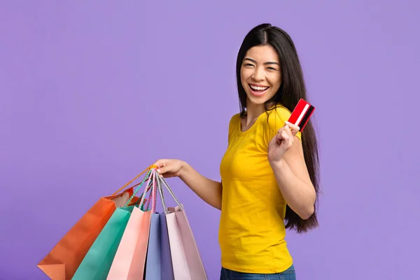 Щасливий шопоголік. Радісна азіатська дівчина з барвистими сумками та кредитною карткою — стокове фото