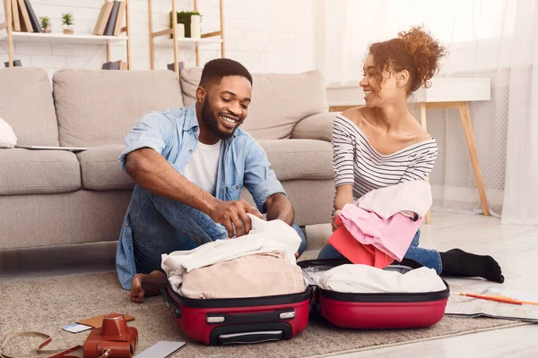 Spouses Packing Clothes In Suitcase Sitting On Floor At Home