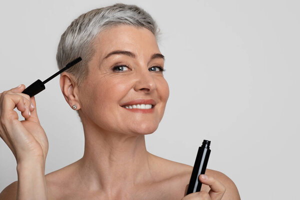 Beauty And Makeup Concept. Portrait Of Smiling Beautiful Middle-Aged Woman Applying Maskara