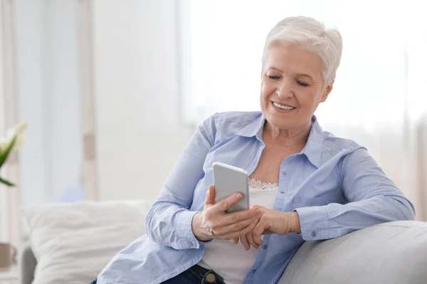 Moderne Technologien für Senioren. Lächelnde ältere Dame nutzt Smartphone zu Hause — Stockfoto