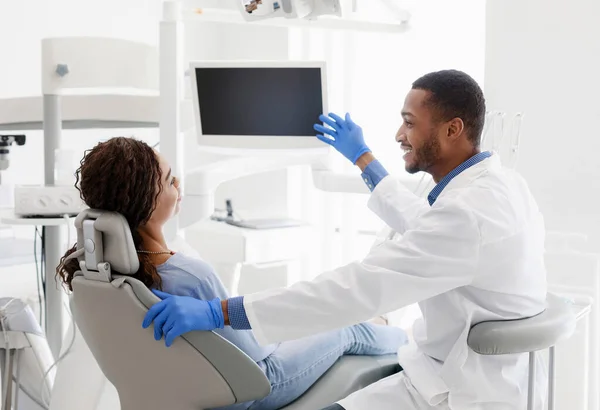 African man dentist talking to patient, pointing at blank monitor — Stock Photo, Image