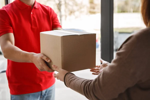 Paketzustellung vom Kurier zum Kunden. Lieferant in roter Uniform schenkt Mädchen Schachtel — Stockfoto