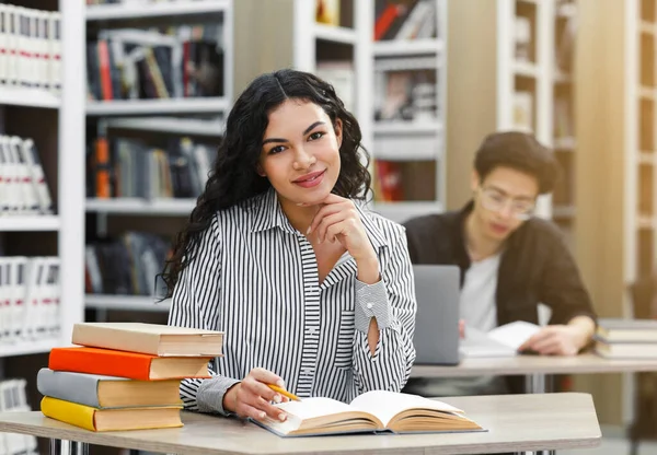 Wesoła latynoska dziewczyna siedzi przy biurku w bibliotece — Zdjęcie stockowe