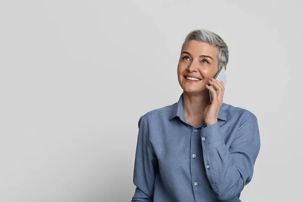 Comunicación moderna. Sonriente mujer de negocios de mediana edad hablando en el teléfono celular sobre fondo de estudio de luz —  Fotos de Stock