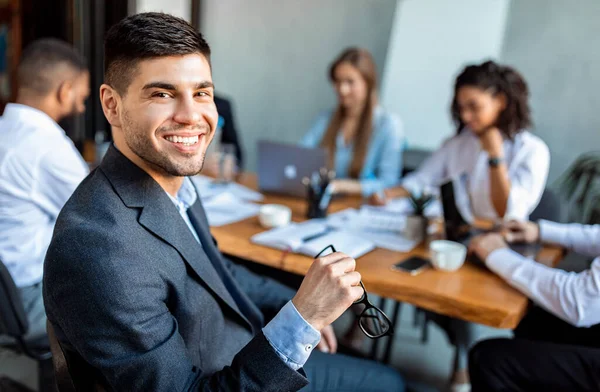 Empresário sorrindo para câmera sentado com parceiros de negócios no escritório — Fotografia de Stock