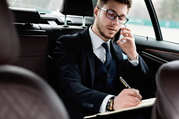 Pengusaha menulis di notebook duduk di mobil mewah — Stok Foto
