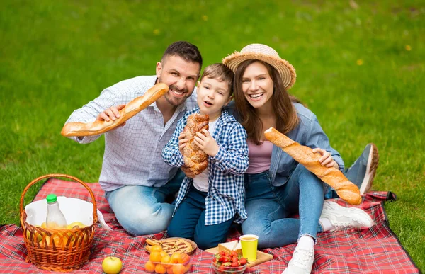 Unga föräldrar med sitt barn äter brödlimpa under familjens picknick på landsbygden — Stockfoto