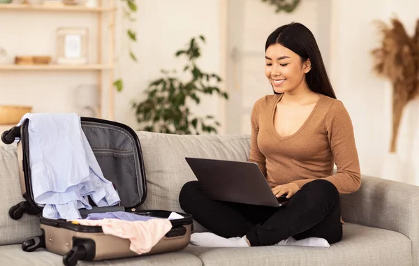 Asyalı Kadın dizüstü bilgisayarını kullanıyor. Bavuluyla içeride oturuyor. — Stok fotoğraf