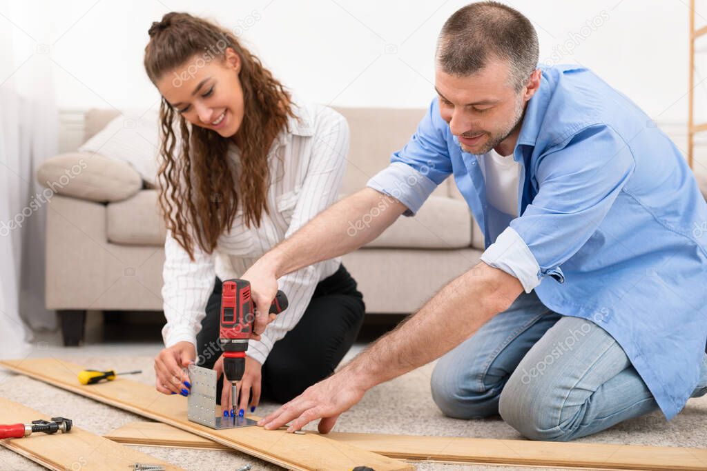 Married Couple Assembling Furniture Together Sitting On Floor Indoors