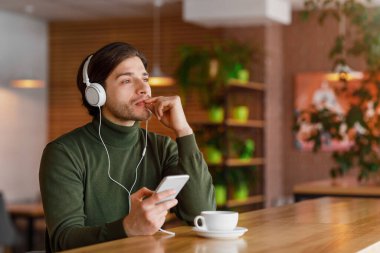 Kulaklıklı, müzik dinleyen, akıllı telefon kullanan düşünceli bir adam.