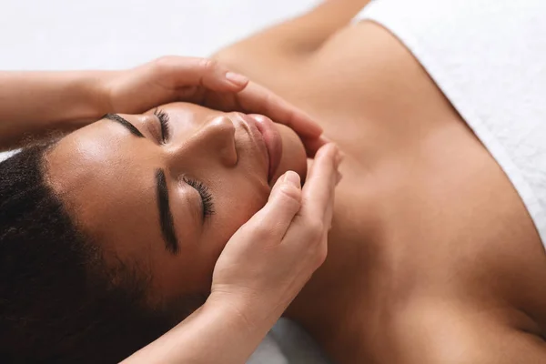 Zbliżenie z terapeuta ręce robi masaż twarzy dla czarny lady — Zdjęcie stockowe