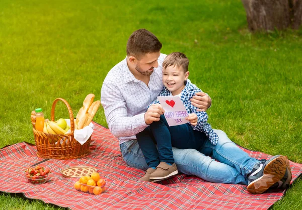 Happy family times. Dad with greeting card and his adorable little boy celebrating fathers day on picnic outside