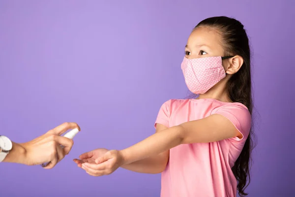 Chica en máscara usando desinfectante aislado sobre la pared del estudio púrpura —  Fotos de Stock