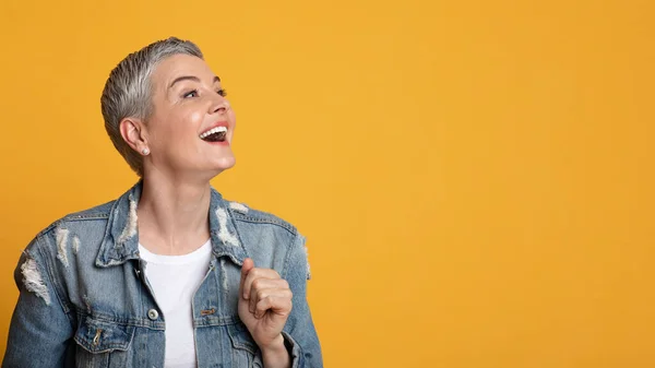 Gran oferta. Emocionada señora de mediana edad mirando el espacio de copia en el fondo amarillo —  Fotos de Stock