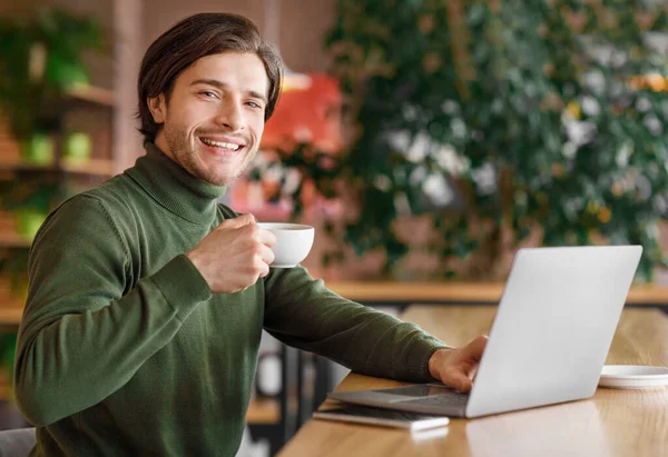 Freelancer positivo trabajando con el ordenador portátil en la cafetería, beber café —  Fotos de Stock