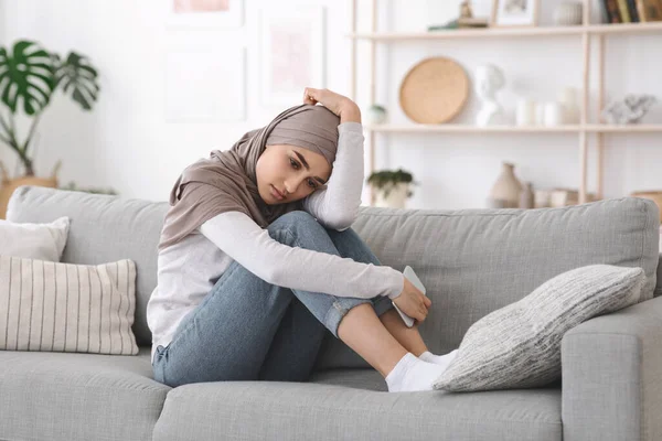 Depressive arabische Frau sitzt zu Hause mit Smartphone in der Hand auf Couch — Stockfoto