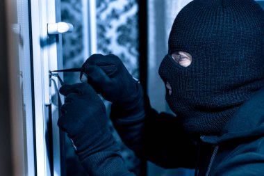 Robber in black balaclava cracking door with metal picklock clipart