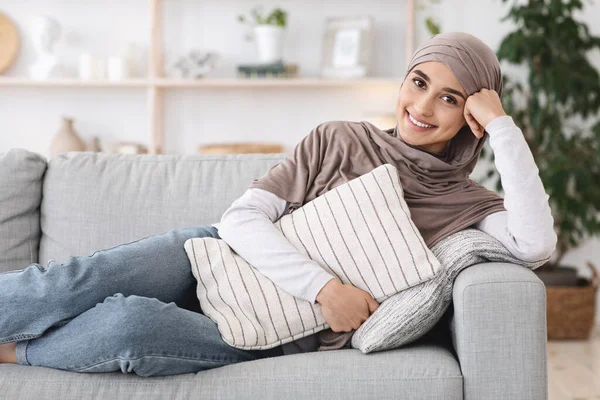 Rumah Tenang. Smiling Arabic Girl In Headscarf Lying On Couch With Pillow — Stok Foto