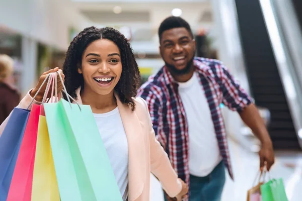 Concepto de ventas estacionales. Emocionada pareja negra disfrutando de compras en el centro comercial juntos — Foto de Stock