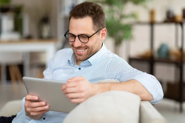 Hombre feliz usando tableta digital sentado en el sofá — Foto de Stock