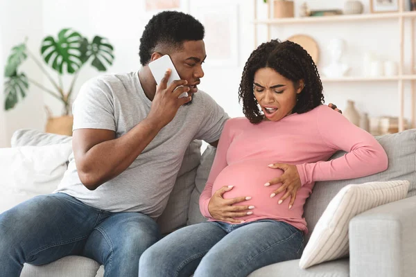 Terhes fekete nő szenved, férj hívja orvos, otthon belső — Stock Fotó