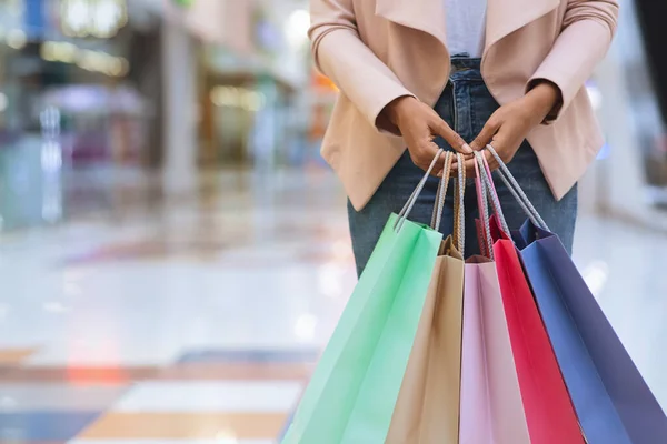Donna nera irriconoscibile in piedi con un sacco di borse colorate nel centro commerciale — Foto Stock