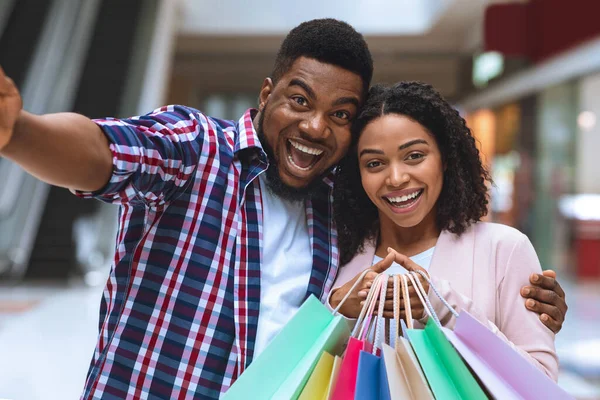 Sales And Consumerism. Excited Black Couple Taking Selfie While Shopping In Mall