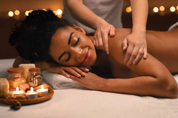 Spa therapist massaging relaxed african woman shoulders