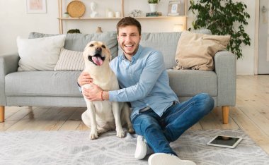 Köpeğiyle yerde oturan mutlu genç adam.