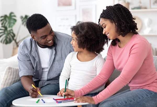 Portret van een gelukkig Afrikaans gezin met een kleine dochter die thuis samen tekent — Stockfoto