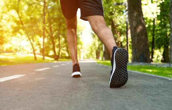 Unrecognizable sportsman running on asphalt road at park on sunny day, close up — Stock Photo, Image