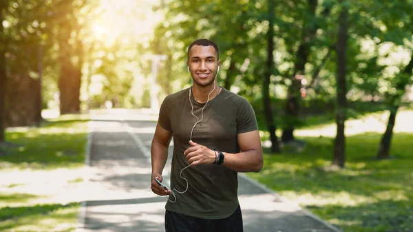 Buon jogger con il cellulare che ascolta musica e si gode la sua corsa al parco la mattina di sole — Foto Stock