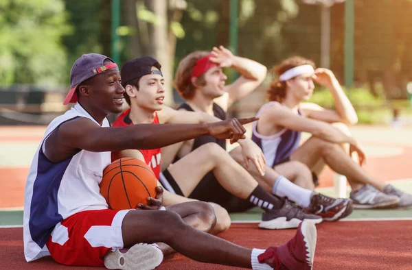 Deportistas milenarios comunicándose durante su descanso en cancha de baloncesto, outdoos. Espacio libre — Foto de Stock