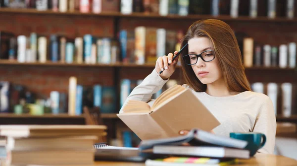 Jonge vrouw in bril leesboek zittend in cafe — Stockfoto