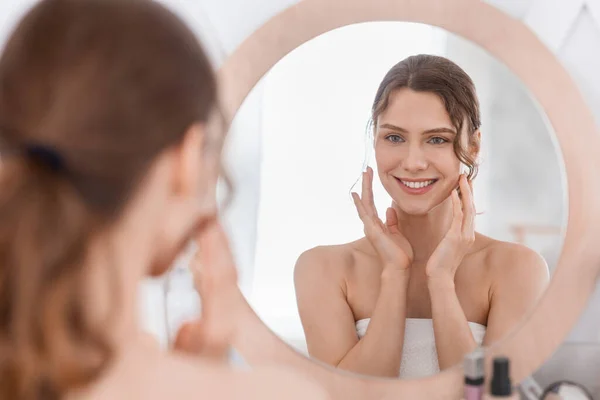 Happy girl enjoying her young smooth skin, looking at mirror — Stock Photo, Image