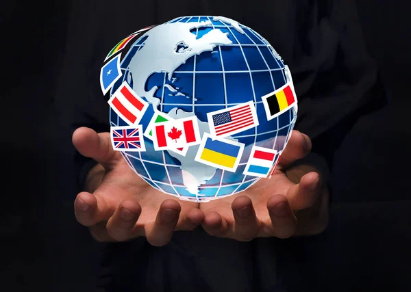 Крупный план человека, держащего планету Земля в окружении международных флагов на черном фоне, коллаж — стоковое фото