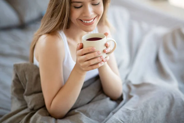 Glimlachend meisje met een kop verse koffie op bed in de ochtend — Stockfoto