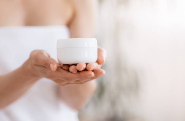 Havluya sarılıp krema kavanozuna sarmalanmış tanınmayan bir kadın.