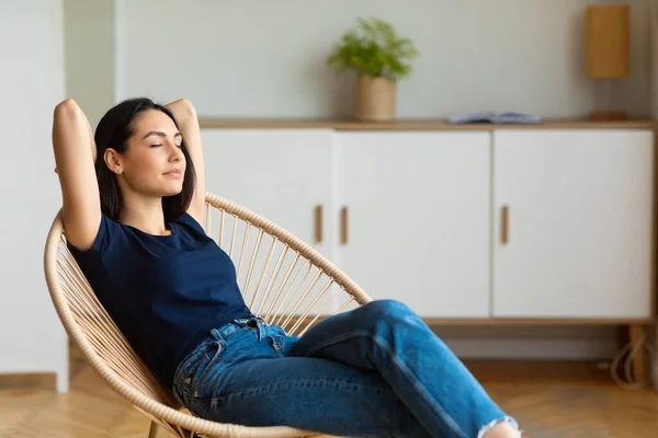 Chica relajante sosteniendo las manos detrás de la cabeza sentada en la silla en interiores — Foto de Stock