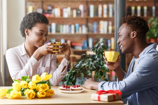 Fête d'anniversaire. Noir gars et fille avec des fleurs et cadeau profiter de leur café au café — Photo