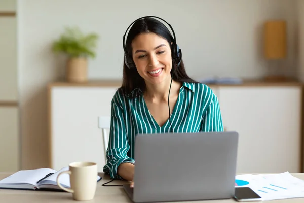 Mujer con auriculares haciendo videollamada sentada en el portátil interior —  Fotos de Stock