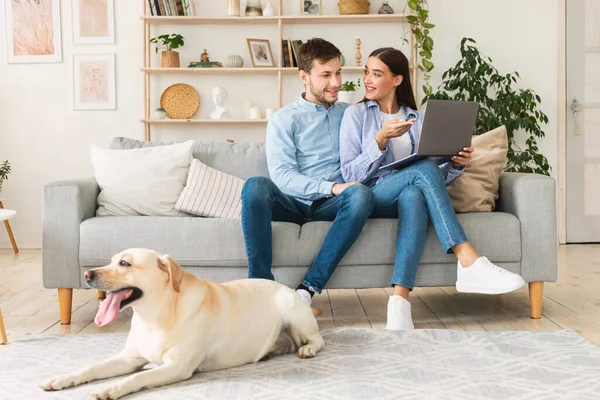 Joven pareja feliz sentado en el sofá con su perro — Foto de Stock