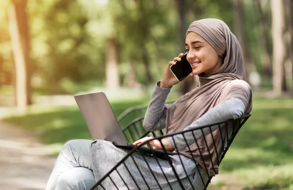 Arab girl in hijab talking on phone and using laptop — Stock Photo, Image