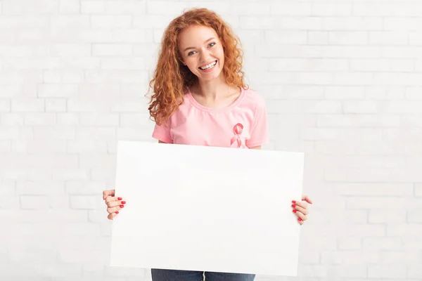 Γυναίκα κρατώντας αφίσσα φορώντας στήθος καρκίνο T-Shirt πάνω από λευκό τοίχο — Φωτογραφία Αρχείου