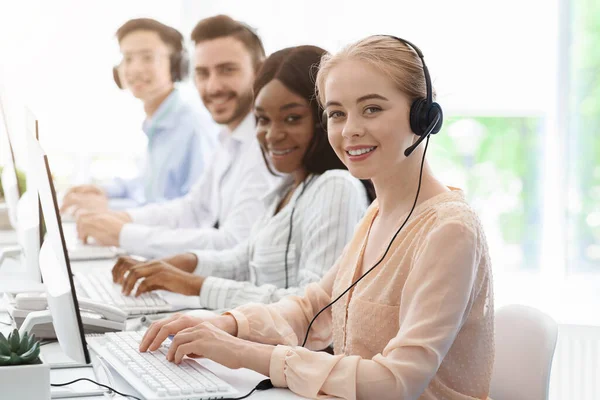 Group of call centre employees smiling and working on computers at light office, copy space