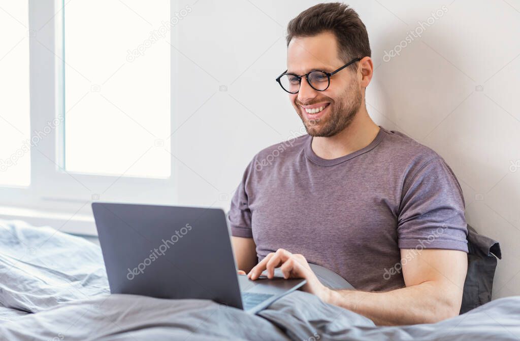 Man Using Laptop Browsing Internet Sitting In Bed At Home
