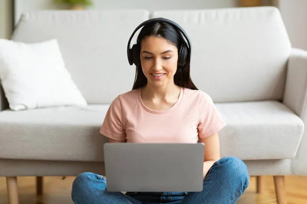 Ragazza millenaria che indossa gli auricolari utilizzando il computer portatile che studia online a casa — Foto Stock