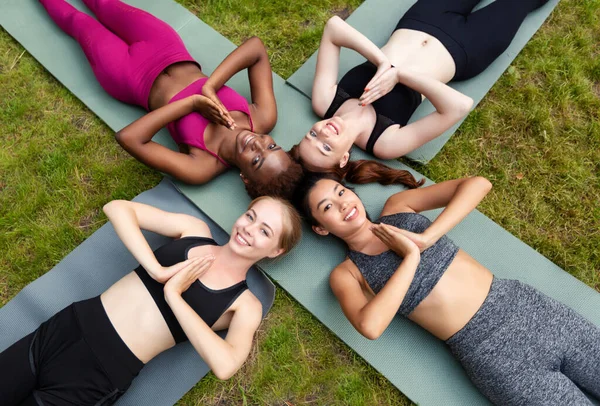 Visão superior de diversas mulheres deitadas em tapetes de ioga e fazendo gesto namaste ao ar livre — Fotografia de Stock