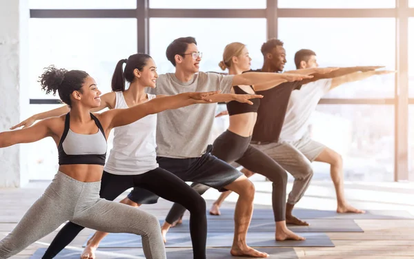 Мультиэтническая группа спортивных людей, практикующих йогу, стоящих в позе Воина 2 — стоковое фото
